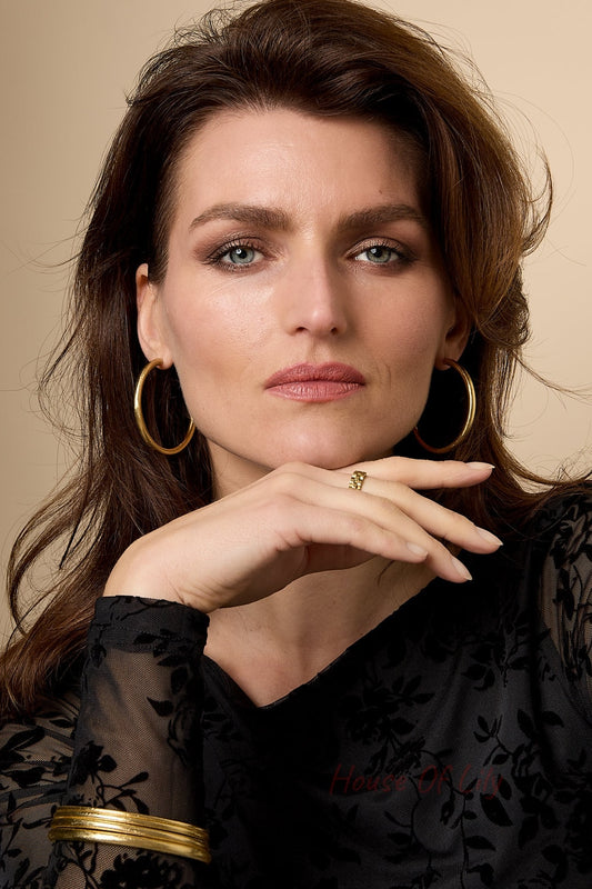 Woman wearing multiple gold circle bangles, including large hoop earrings and a gold ring, styled with a black floral lace top