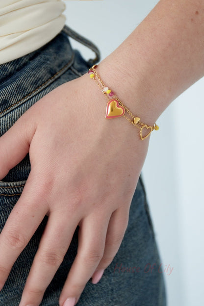 Close-up of a woman's wrist wearing a gold-plated heart charm bracelet with pink and yellow beads paired with denim jeans