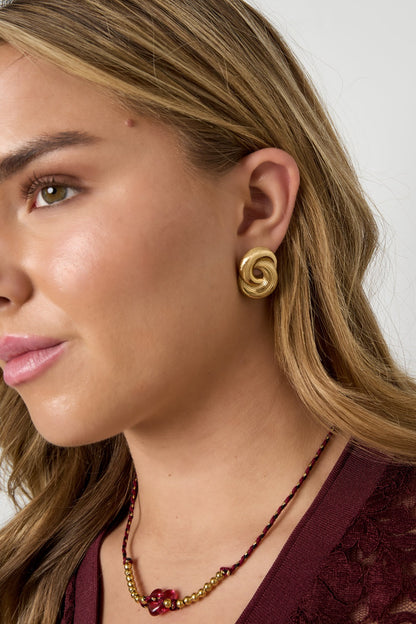 Model wearing gold twist statement stud earrings paired with a burgundy lace top and beaded necklace
