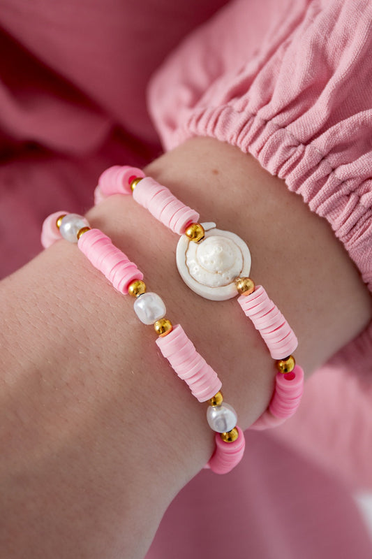 Close-up of two pastel pink shell charm beaded bracelets worn on wrist with pink sleeve