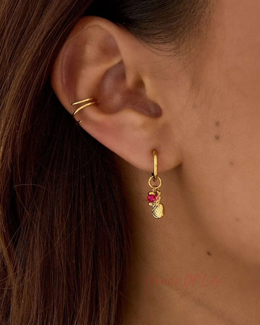 Gold hoop earring with a small gold pineapple charm and a vibrant pink crystal drop, worn on an earlobe.