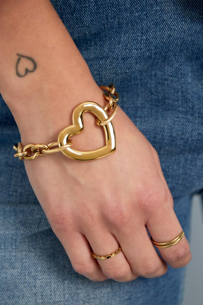 Close-up of a woman’s wrist wearing the chunky gold heart link bracelet paired with rings, styled with denim jeans