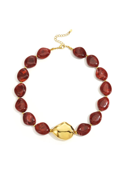 Close-up flat lay of deep red acrylic beaded necklace with polished gold irregular centerpiece on white background
