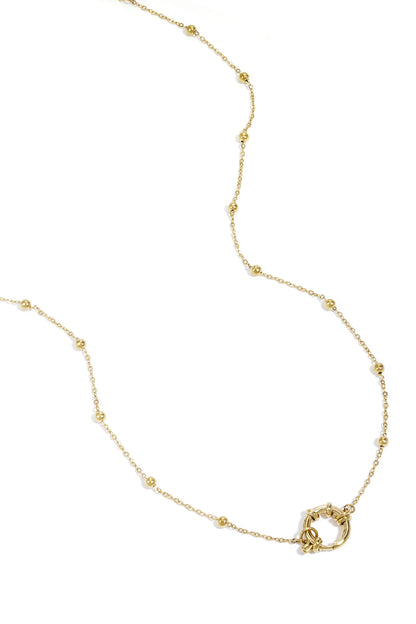 Close-up of delicate gold chain necklace with small round beads and circular clasp against white background