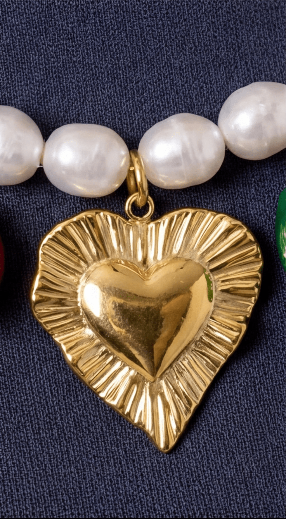 Gold heart-shaped pendant on a necklace with pearls against a dark background