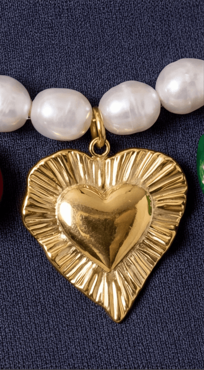 Gold heart-shaped pendant on a necklace with pearls against a dark background