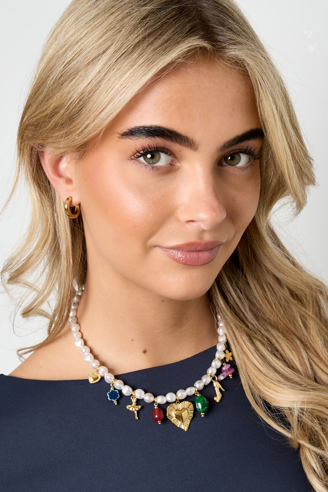 Portrait of a smiling blonde woman wearing the pearl charm necklace and gold hoop earrings, highlighting the youthful and aesthetic jewelry style