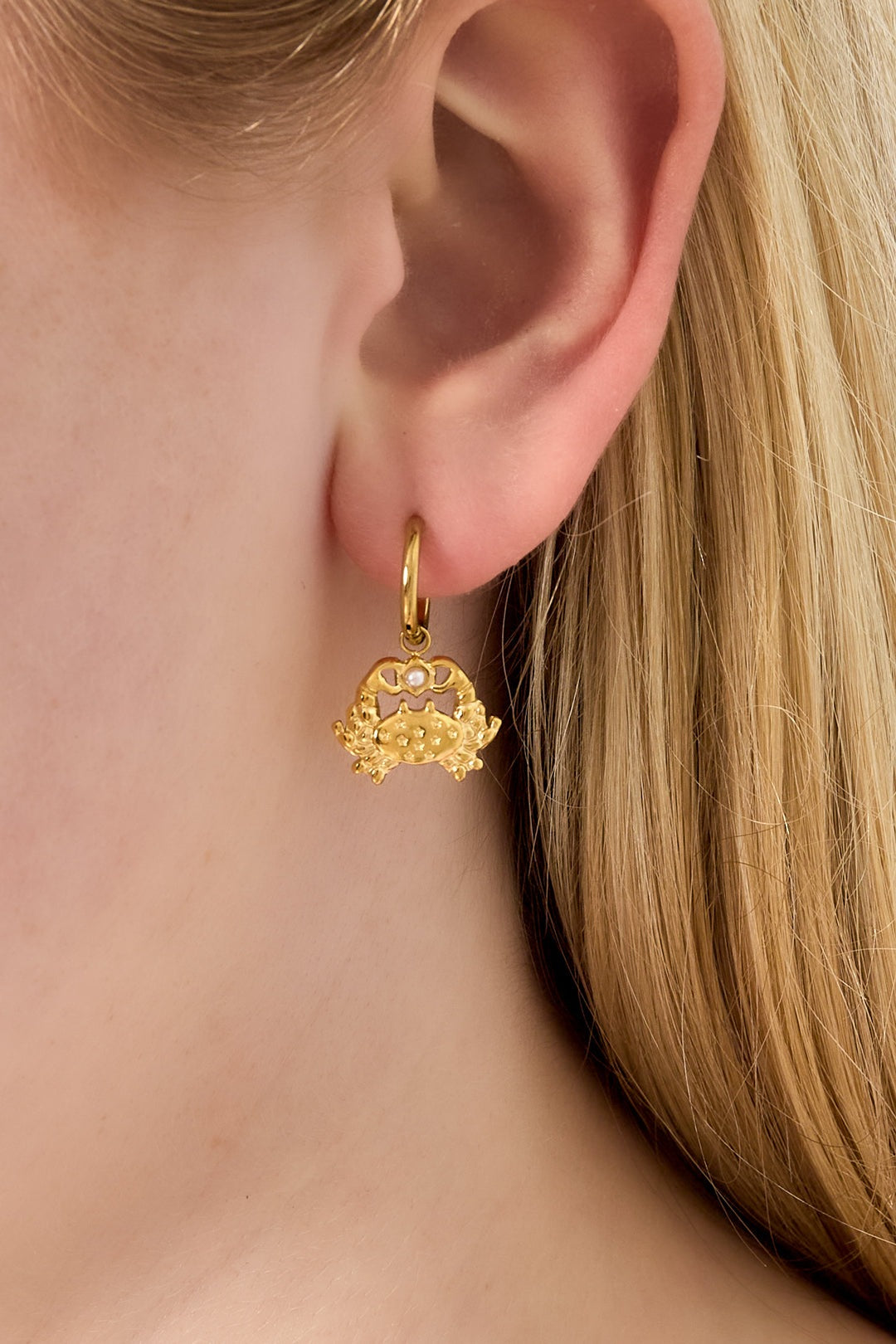 Close-up of gold crab drop hoop earring worn by model with blonde hair.