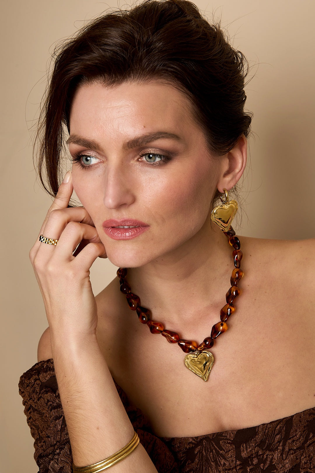 Woman wearing amber beaded necklace with gold heart pendant and matching heart earring, styled with brown off-shoulder top