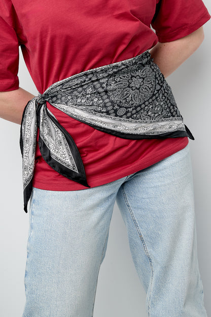 Woman wearing black and white paisley scarf tied stylishly around waist over red top and light blue jeans