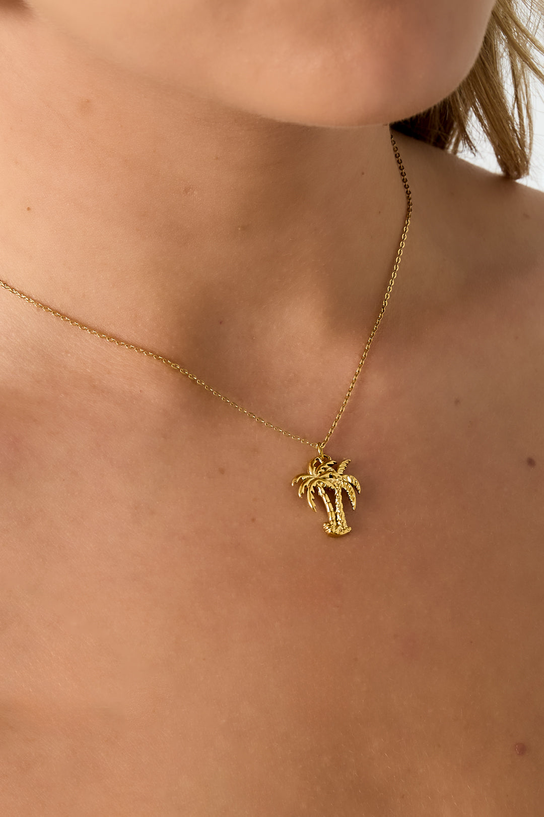 Close-up of palm tree pendant necklace worn around a woman's neck showcasing the delicate gold chain and charm