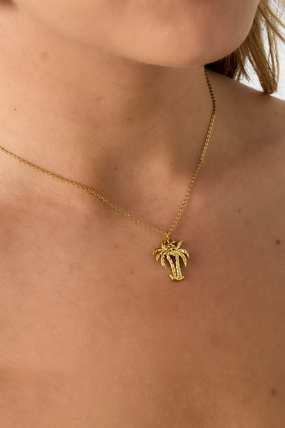 Close-up of palm tree pendant necklace worn around a woman's neck showcasing the delicate gold chain and charm