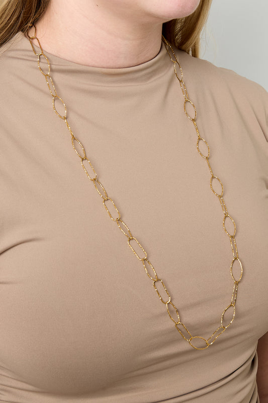 Model wearing long gold textured link chain necklace with no pendants over beige top