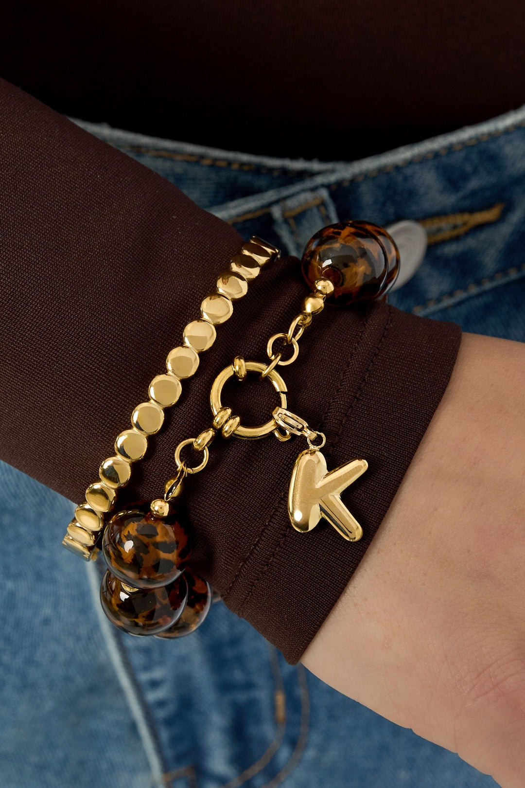 Close-up of wrist wearing gold and tortoise shell bead bracelets, one with letter K charm