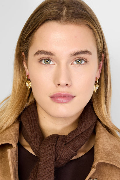 Young woman with blonde hair wearing gold heart charm hoop earrings and brown scarf