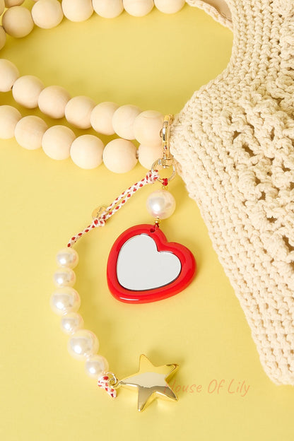 Heart charm with mirror, pearl beads, and star attached to wood-beaded handle of crochet bag on yellow background