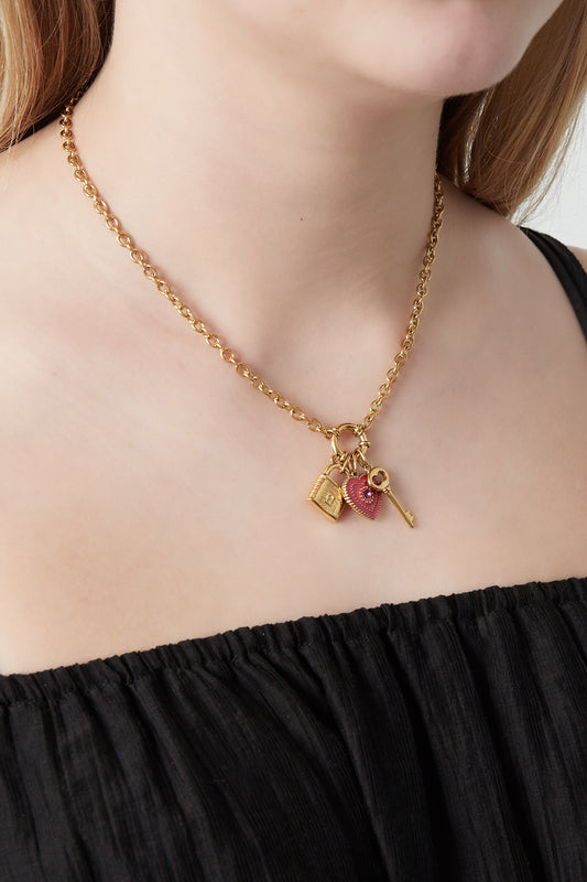 Woman wearing the gold-plated charm pendant necklace featuring a red heart, golden padlock, and key charms against a black top