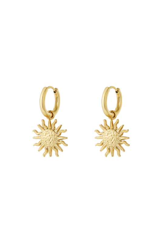 Pair of gold drop hoop earrings with textured sun charm pendants on white background