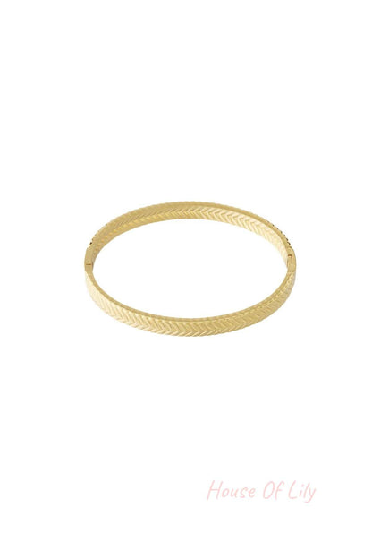 Gold bangle bracelet with herringbone texture on a white background