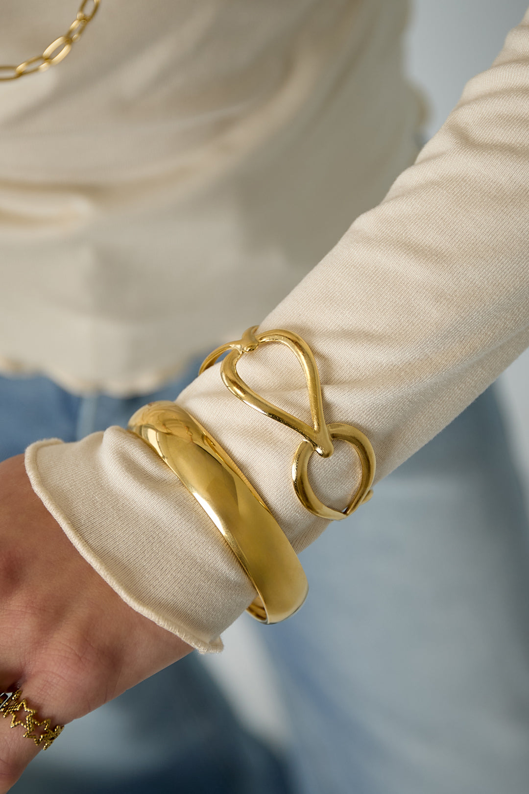 Woman wearing gold open loop cuff bracelet paired with polished gold bangle on wrist with cream top
