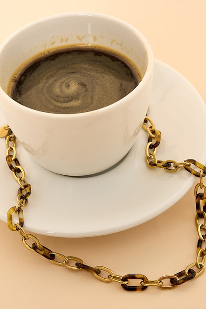 Close-up of tortoise link chain necklace draped around a white coffee cup on a saucer.