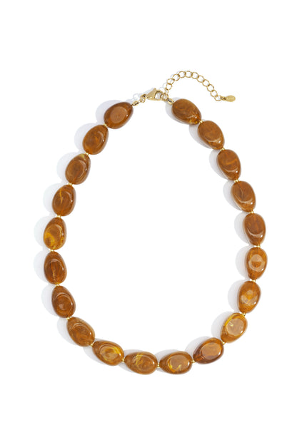 Chunky necklace with glossy, amber-toned marbled resin oval beads on a gold-tone metal chain, isolated on white.