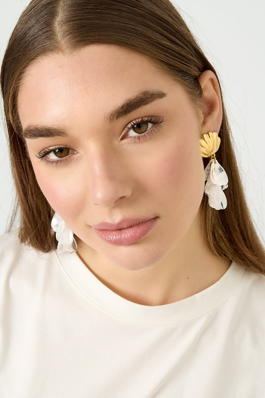 Model wearing gold shell earrings with white translucent petals, close-up view
