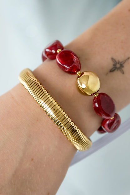 Close-up of chunky red acrylic beaded bracelet with gold bead on wrist alongside gold coil bracelet
