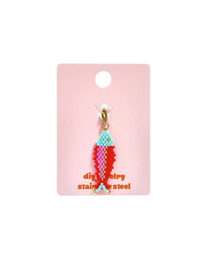 Glass fish charm on a pink display card, featuring red, pink, light blue, and gold seed beads.