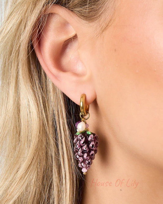 Side profile of a woman displaying a single gold hoop earring with a detailed glass grape charm, highlighting craftsmanship