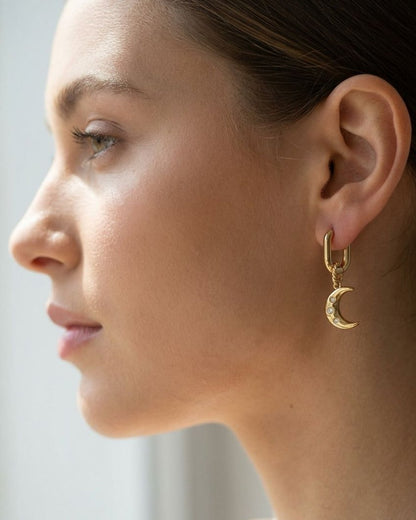 Celestial sun and moon drop earrings featuring zircon accents worn on an earlobe in soft natural lighting.