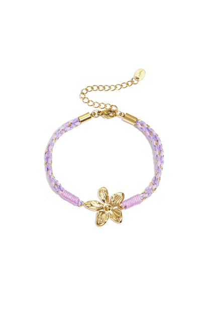 Close-up of lavender braided rope bracelet with gold flower charm and adjustable chain clasp on white background