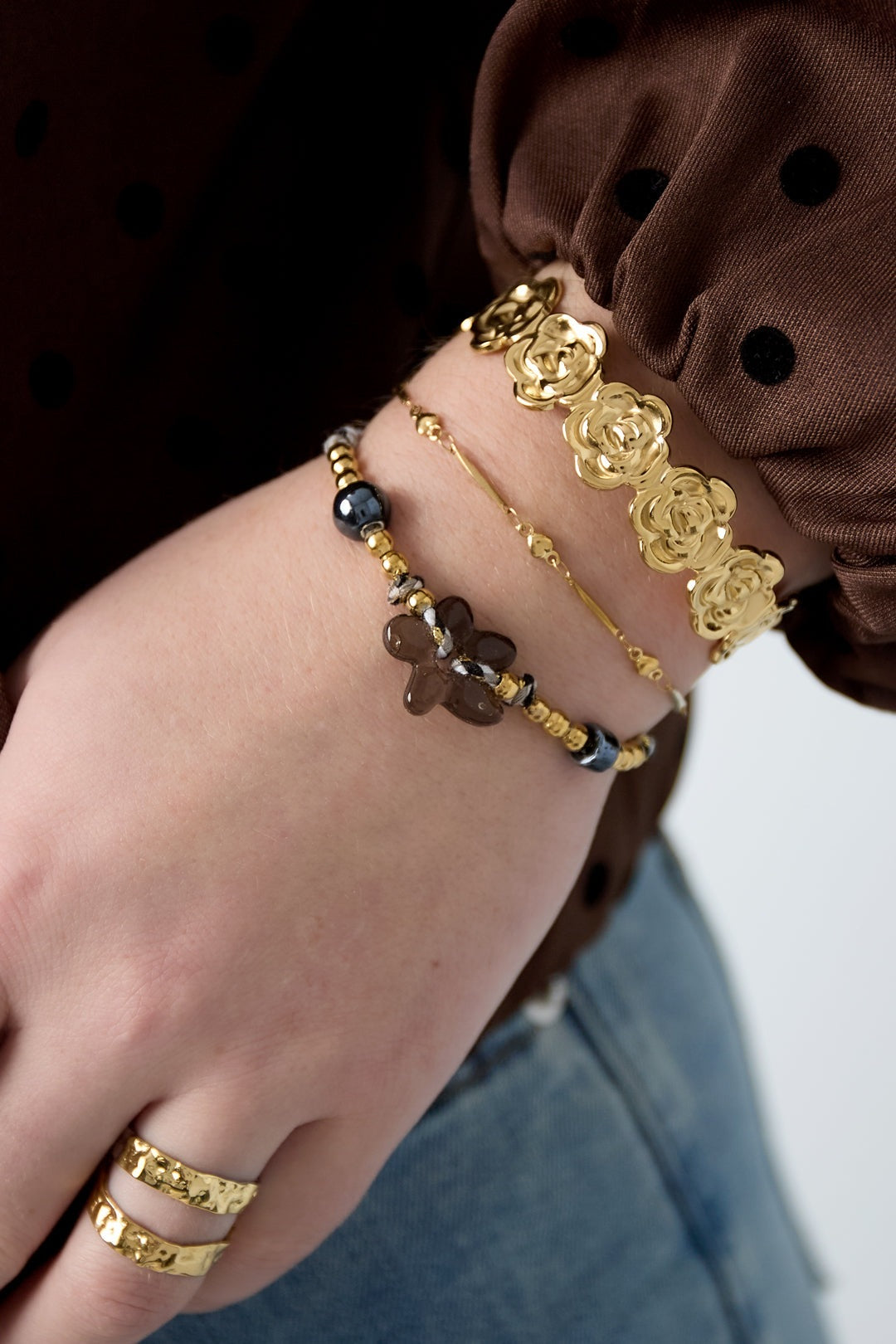 Styled wrist shot showing layered bracelets, including a gold heart link bracelet paired with textured and beaded bracelets and rings.