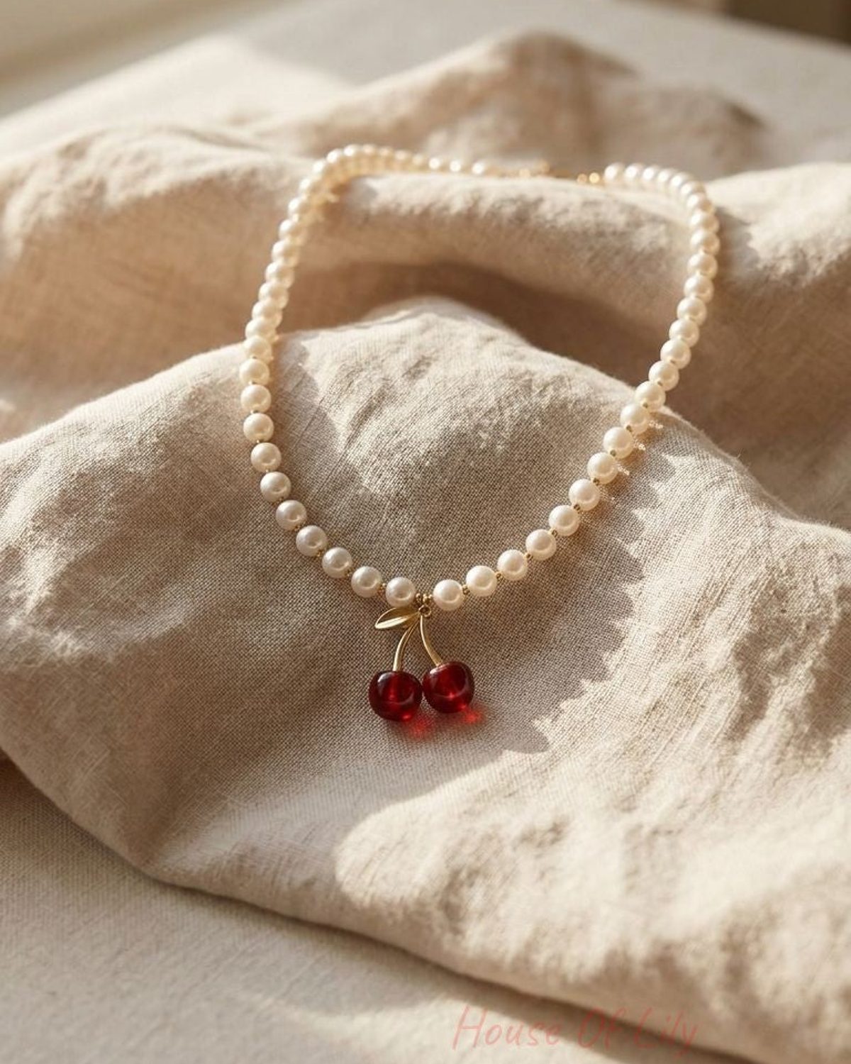 Close-up of the Cherry Charm Pearl necklace with imitation pearls and gold-tone cherry charm on soft fabric, highlighting its delicate details.