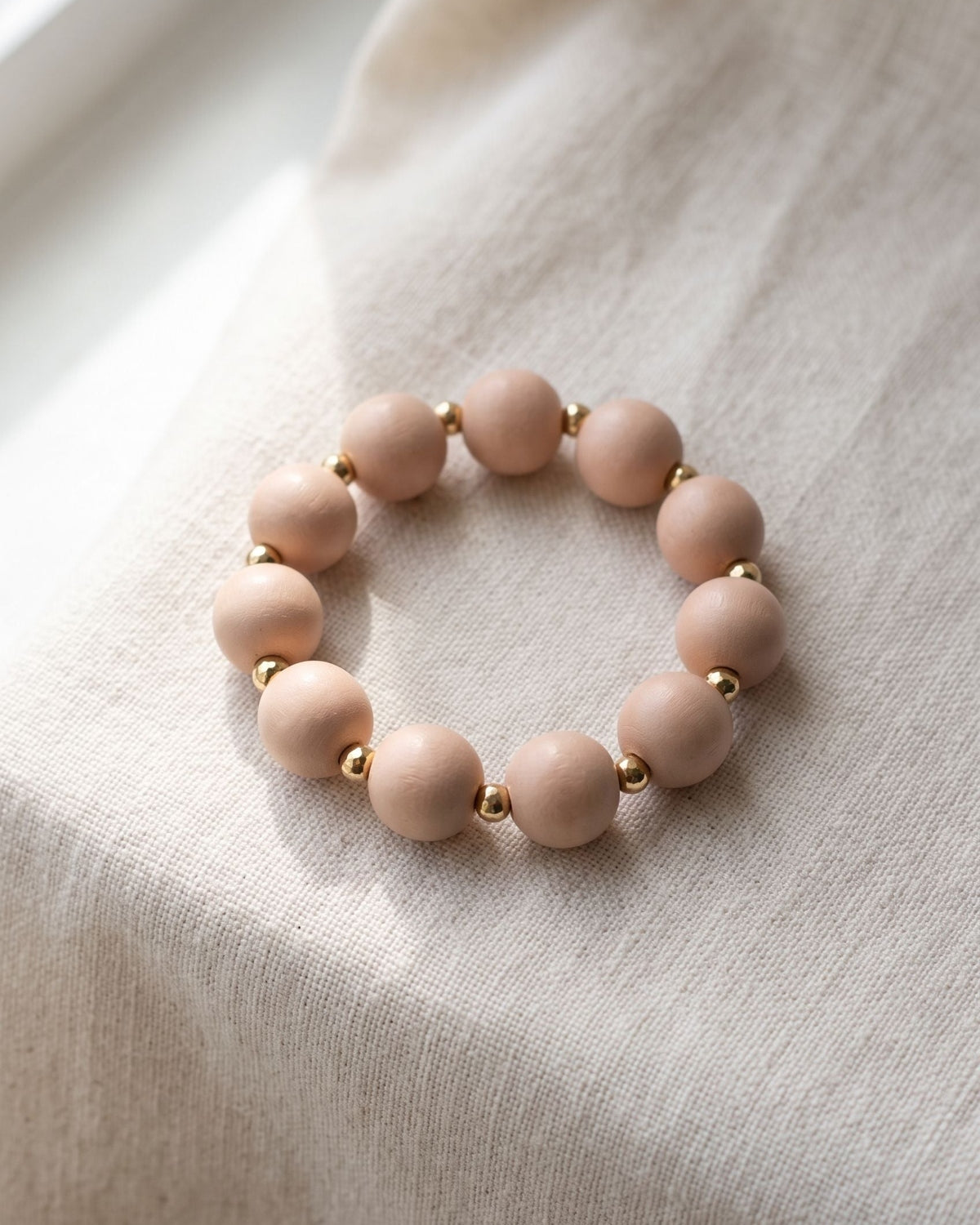 Dainty wooden beaded bracelet featuring brown and pink beads resting on soft off-white linen fabric.