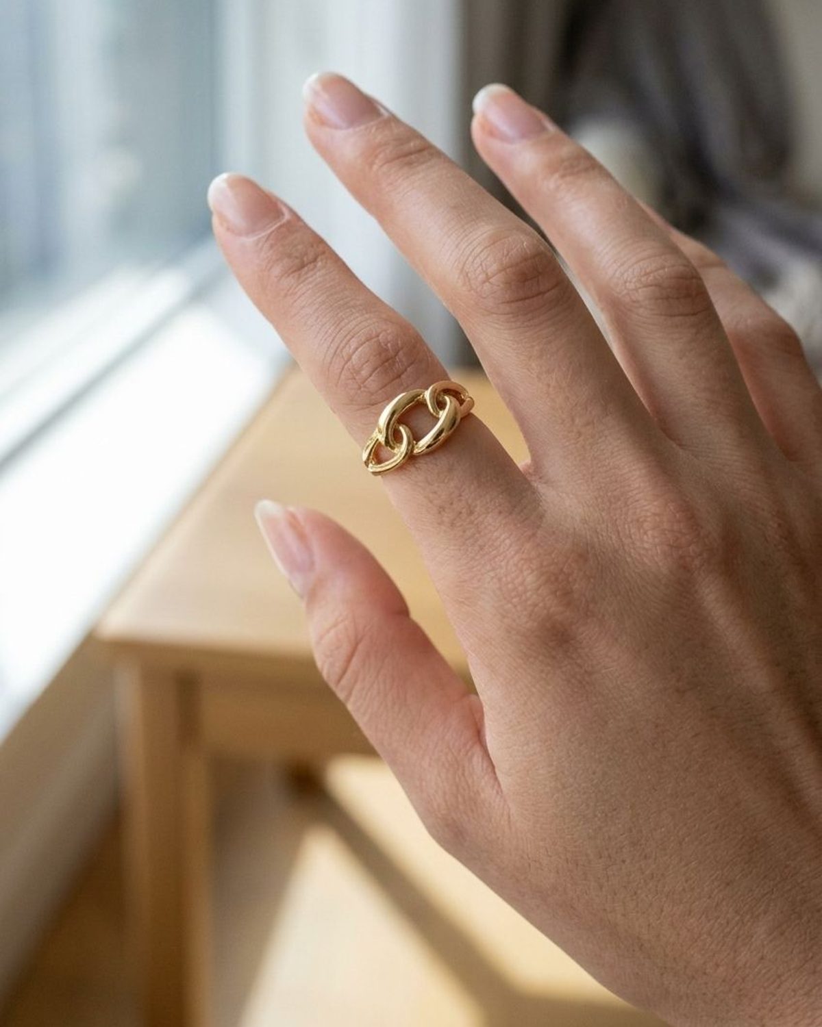 Chunky gold-plated chain link statement ring worn on a finger, showcasing an irregular industrial design.