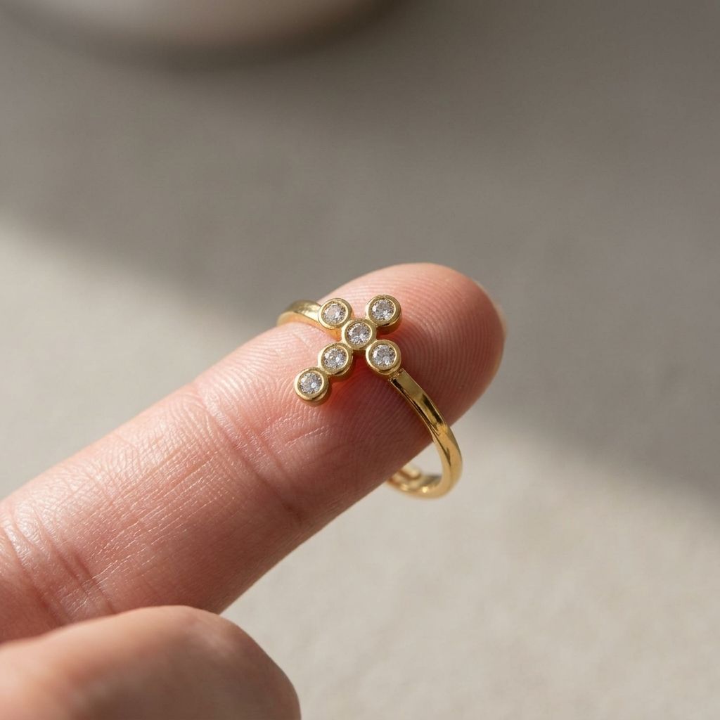 Close-up of a small gold-plated cross ring with rhinestones on a woman's fingertip, highlighting its sparkle and delicate design.
