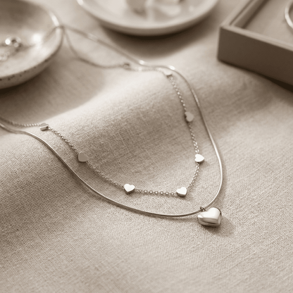 Ultra-sharp close-up of the delicate heart layered necklace highlighting fine craftsmanship, micro-texture, and silver shine on a blurred neutral background.