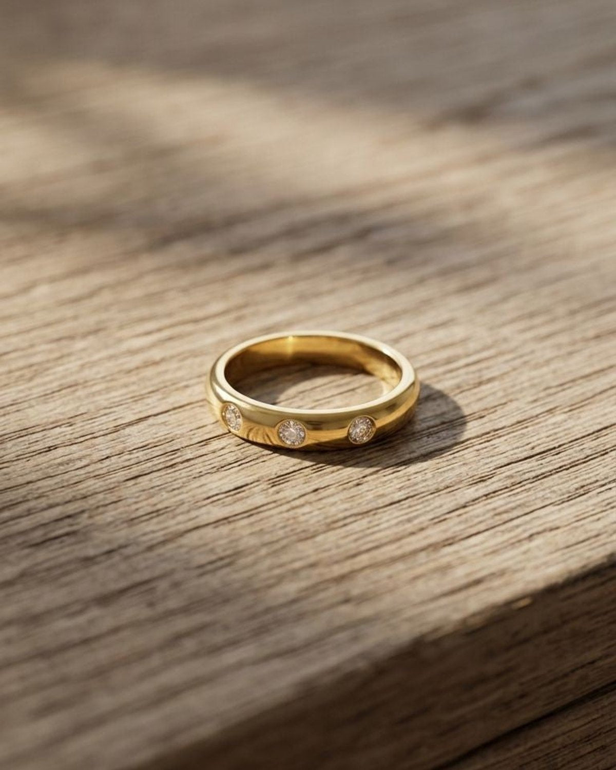 Close-up of the delicate gold-plated stainless steel ring with three zircon stones on a wooden surface, highlighting its subtle sparkle.