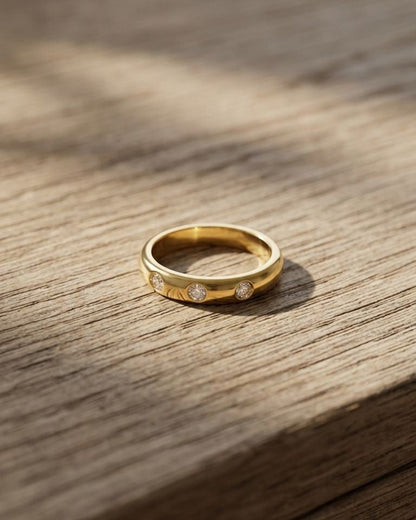 Close-up of the delicate gold-plated stainless steel ring with three zircon stones on a wooden surface, highlighting its subtle sparkle.