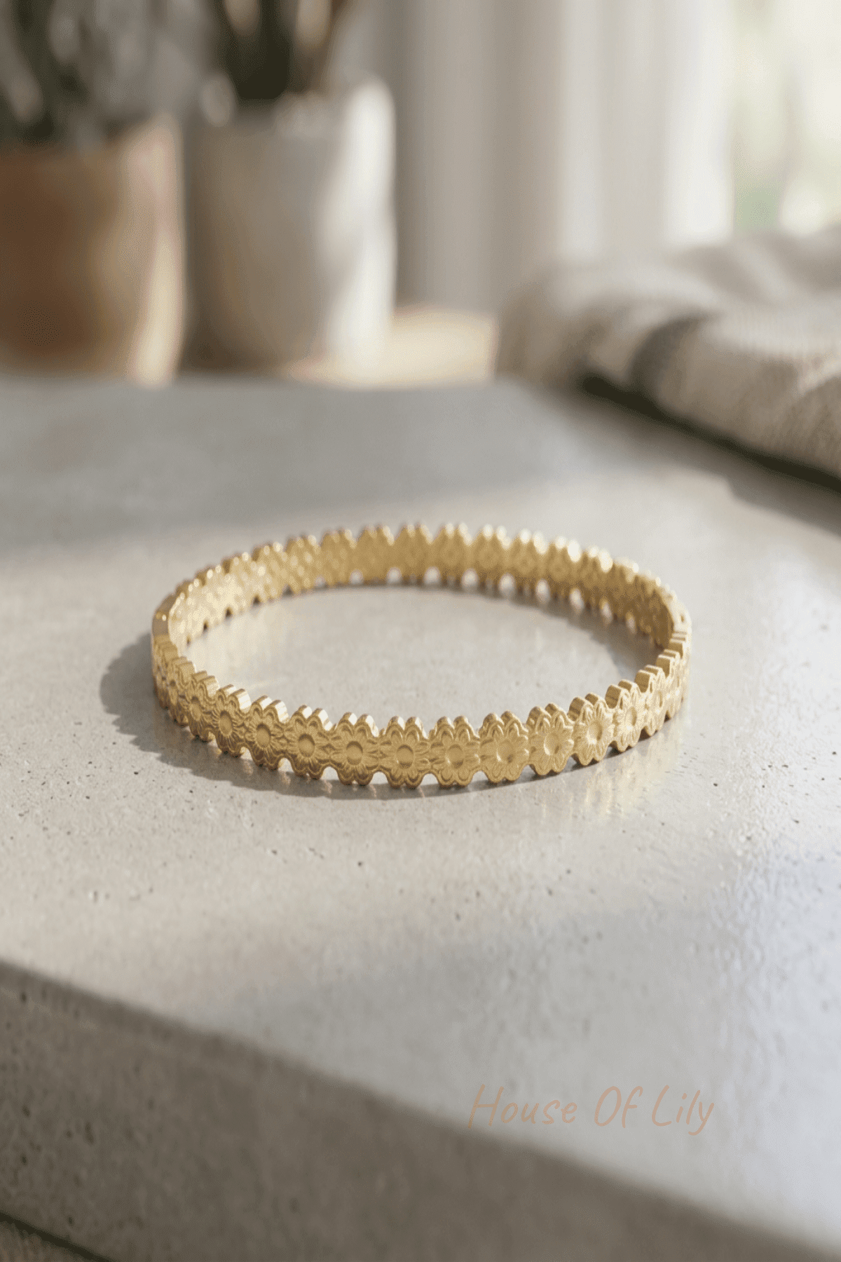 Close-up of a gold-tone stainless steel floral engraved bangle bracelet highlighting intricate details and smooth finish on a reflective surface.