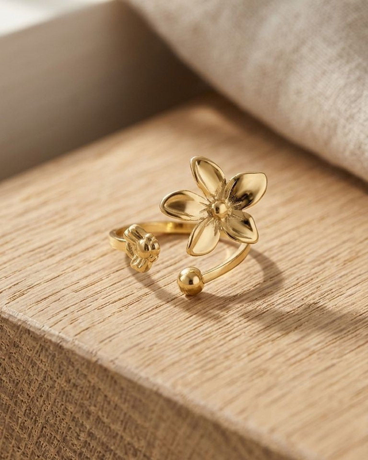 Close-up of the Gilded Petal Statement ring with double-flower design, gold-tone metal, and bead detail on a wooden surface.
