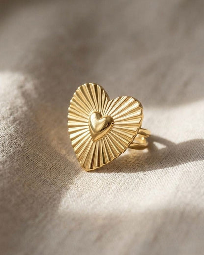 Close-up of the Golden Sunburst Heart statement ring with sunburst etchings and gold finish on neutral fabric, highlighting its intricate design.