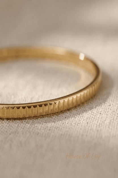 Detailed macro shot of a gold stainless steel textured bangle highlighting groove details and polished surface with warm lighting.