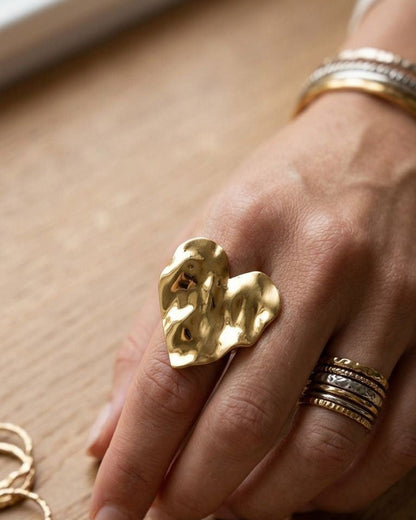 Close-up of the tiny brushed Lily Heart statement ring on a textured wooden surface with soft lighting highlighting its matte finish.