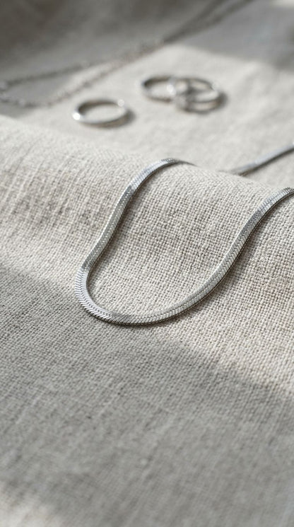 Close-up of the silver-plated stainless steel layered necklace on linen fabric, highlighting its sleek flat link pattern and high shine.