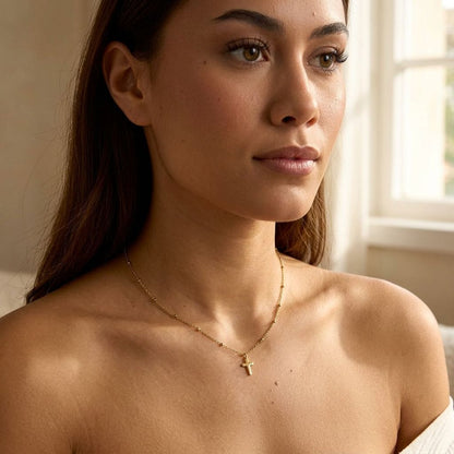Close-up of stainless steel 'Cross My Heart Chain' with minimalist cross pendant on a model's neck in a softly lit cozy setting.
