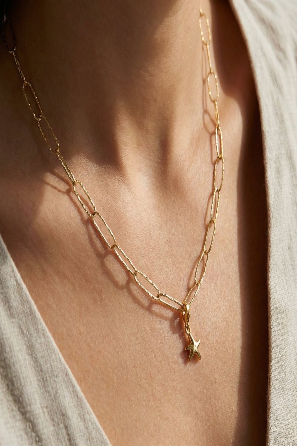 Ultra-detailed close-up of textured paperclip chain necklace with hammered finish, delicately shimmering surface on a neutral fabric backdrop.