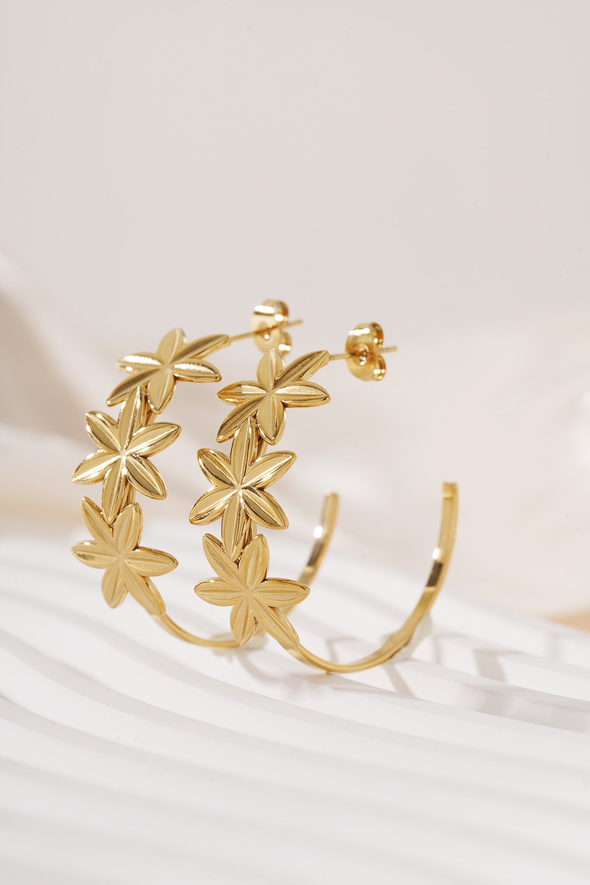 Gold floral hoop earrings standing on a white textured surface