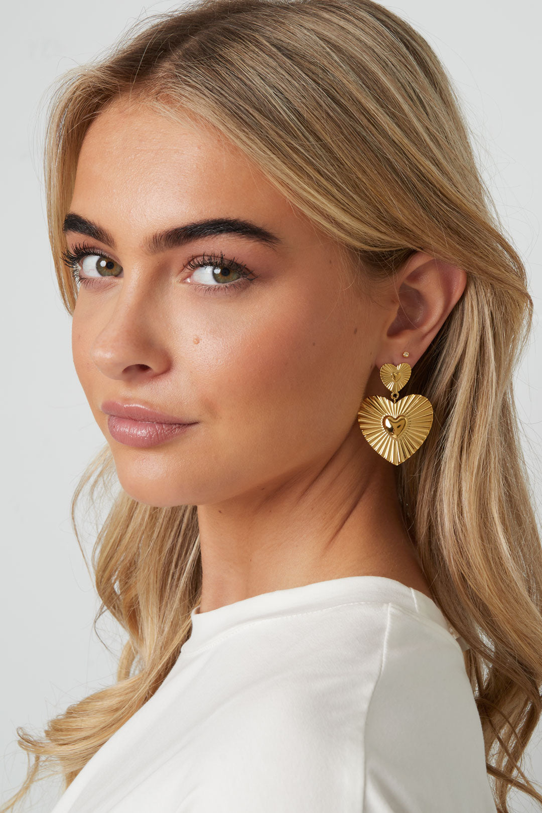 Close-up of a woman wearing gold heart-shaped drop earrings with a soft, youthful look